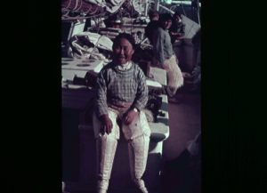 Image of Inuit woman sitting, aboard. Men beyond  [purple]