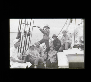 Image of Crew mid-ship, in foul weather gear. One has accordian;one uses spy-glass [b&w]