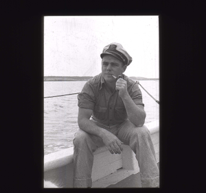 Image: Crewman with pipe, sitting on rail  [b&w]