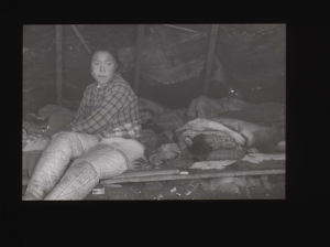Image of Inuit woman sittiing in tupik; child sleeping on platform  [b&w]