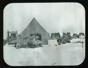 Image: Large tent. Two Inuit men seated on furs, one using binoculars, one with pipe...