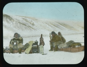 Image of Three men sitting on sledges drinking tea. Teakettle, stove, mugs, supplies