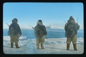Image of Three men watching iceberg. Each has coil of line on his back