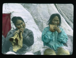 Image of Nelle-ka-tee-ah and Nelle-ka sitting outside tupik chewing skins