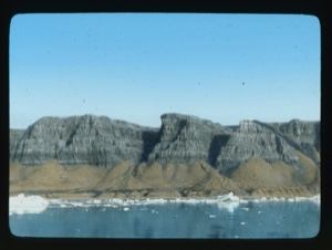 Image: Large sand piles against striated cliffs. Ice floes at edge
