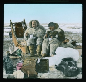 Image: Elmer Ekblaw and Inuit man [Esayoo] sitting on sledge to eat. Tea kettle near