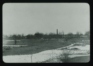 Image: Wintry landscape with orchard. Buildings and smoke stack beyond       