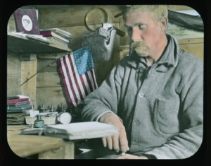 Image: Harrison Hunt seated at desk reading. Small flag and books near