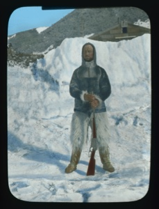 Image: Jot Small standing on snow, leaning on rifle....