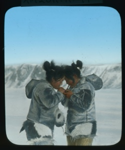 Image: Two inuit women, foreheads together, lighting cigarettes