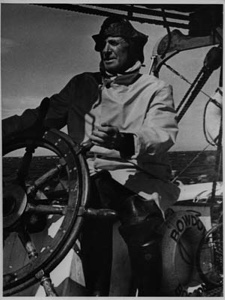 Image of Donald MacMillan at the BOWDOIN's wheel, in foul weather gear