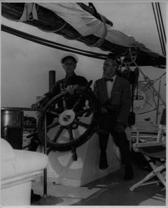 Image of Donald MacMillan and ? sitting at the BOWDOIN's wheel after arriving in Mystic