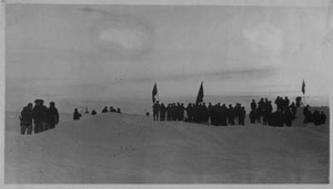 Image: Large group of men on snow with flags, cameras; some wear polar bear pants. Soviet Polar Expedition