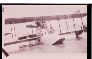 Image of Two men sit on wing of bi-plane, in water