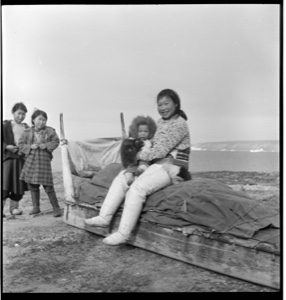 Image of Eskimo [Inuit] woman and child on sledge, girls beyond