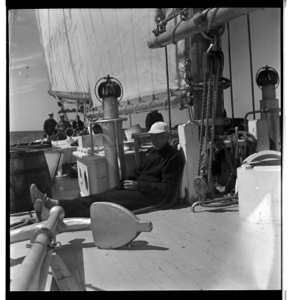 Image of John Bodet sitting on deck near anchor, others beyond at wheel