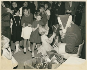 Image of Santa Claus, seated, with girl talking to him as other children look on; Thule AFB