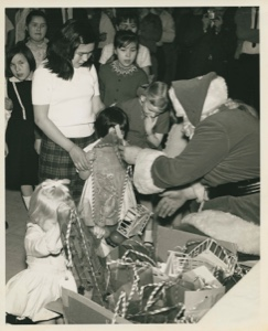 Image of Santa Claus with child and mother, gifts in a bin; Thule AFB