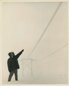 Image: Man pointing to wires running from low support, during snow storm. Thule AFB