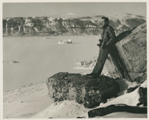 Image of Harold Grundy (?) looking across ice to iceberg & mountain