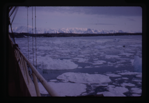 Image of Sip moving through drift ice, snowy mountains in distance