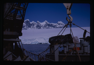 Image of Dinghy held by crane. Mountains and glacier in background.