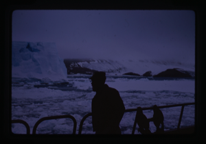 Image of Man standing on ship loking at iceberg