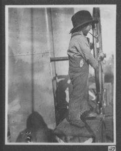Image of Eskimo boy, with pipe, at wheel