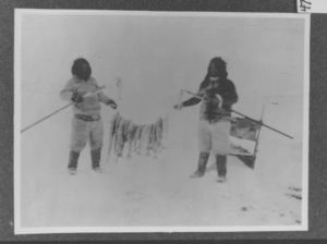 Image of Eskimos with string of fish and fishing spears