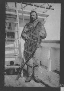 Image of Thomas Gushue (?) on deck in furs, holding snowshoes