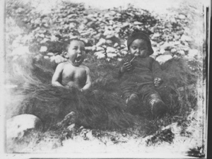 Image of Tahtarah, yawning, and Wewe''s boy  with pipe, sitting on grass - 