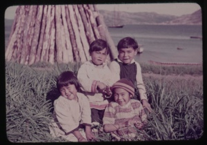 Image: Four Eskimo [Inuit] children in grass by firewood stack