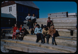 Image: Group of Eskimos [Inuit] sitting on stacked lumber