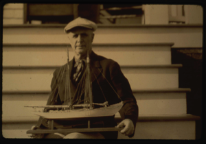 Image: Donald MacMillan seated on his steps holding model of the Bowdoin