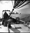 Image of Miriam at wheel, iceberg beyond. Melville Bay