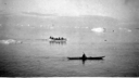 Image of Eskimos [Inuit] in an open boat, and a kayaker