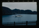Image of The Bowdoin moored near mountain. Picket fence in foreground