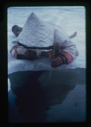 Image of Inuit man prone on snow, fishing with jig