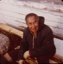 Image of Eskimo [Inuk] man sitting by boat