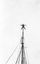 Image of Donald MacMillan spread-eagle on mast peak