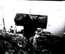 Image of Inuit man carrying wooden crate from ship on his back