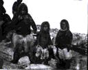 Image of 3 young Inuit boys in polar bear pants. Adults beyond.