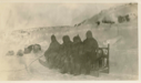 Image of Crew in furs, sitting on sledge. Dogs at rest