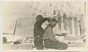 Image of Ralph Robinson getting a haircut on deck. Fox skins hanging
