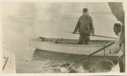Image of Thomas McCue in small boat, holding harpoon. Inuit near using harpoon
