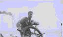 Image of Crewman at wheel. Two more sitting by