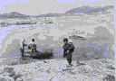 Image of Eskimos [Inuit] at water's edge; two men working in boat; girl carries child