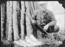 Image of ? with pole and four fish, by wood stack