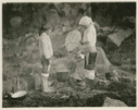 Image of Maligiak. Two Eskimo [Inuit] women standing beside a fire where they are boiling some fish (halibut).