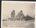 Image of E-took-a-shoo (Ittukusuk) and Ak-Pood-a0shah-o putting [...] king dog on sledge [Two Inuit men with dog. Sledge, snowshoes, crates near ]
